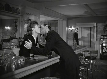 Movie still from “Mildred Pierce” (1945), directed by Michael Curtiz – A man and a woman kissing at a bar; Wide shot, High angle