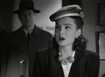 Movie still from “Mildred Pierce” (1945), directed by Michael Curtiz – A woman wearing a hat and a bow tie in front of a man in a suit; Close Up shot, Over the shoulder angle
