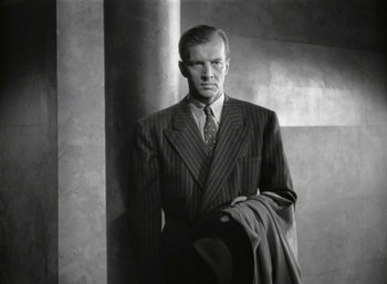 Movie still from “Mildred Pierce” (1945), directed by Michael Curtiz – A black and white photo of a man in a suit and tie; Medium shot, Low angle