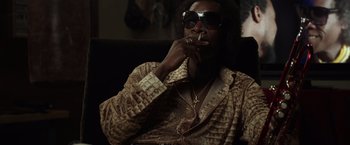 Movie still from “Miles Ahead” (2015), directed by Don Cheadle – A man smoking a cigarette while sitting on a couch; Medium shot, Low angle