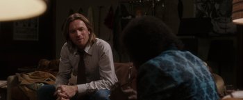 Movie still from “Miles Ahead” (2015), directed by Don Cheadle – A man sitting on a couch talking to another man; Medium shot, Over the shoulder angle