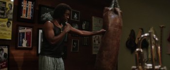 Movie still from “Miles Ahead” (2015), directed by Don Cheadle – A man is boxing in a room with pictures on the walls; Medium shot, Low angle