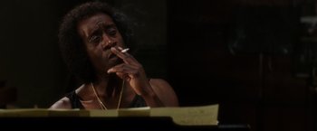 Movie still from “Miles Ahead” (2015), directed by Don Cheadle – A man smoking a cigarette while sitting at a table; Close Up shot, Low angle