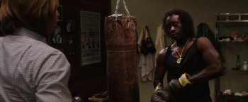 Movie still from “Miles Ahead” (2015), directed by Don Cheadle – A man standing next to a brown punching bag; Medium shot, Low angle