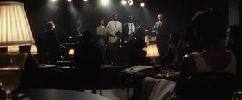 Movie still from “Miles Ahead” (2015), directed by Don Cheadle – A group of men on a stage with a saxophone; Extreme Wide shot, High angle
