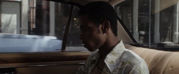 Movie still from “Miles Ahead” (2015), directed by Don Cheadle – A man sitting in the back seat of a car looking out the window; Close Up shot, Over the shoulder angle