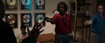 Movie still from “Miles Ahead” (2015), directed by Don Cheadle – A man in a red shirt is holding a gun; Medium shot, Over the shoulder angle