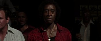 Movie still from “Miles Ahead” (2015), directed by Don Cheadle – A man in a red shirt and a gold cross necklace; Close Up shot, Low angle
