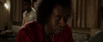 Movie still from “Miles Ahead” (2015), directed by Don Cheadle – A person with a red shirt is sitting down and looking down; Close Up shot, Low angle