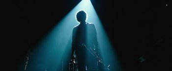 Movie still from “Miles Ahead” (2015), directed by Don Cheadle – A man holding a guitar standing in the middle of a stage; Medium shot, Low angle