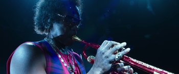 Movie still from “Miles Ahead” (2015), directed by Don Cheadle – A man playing a trumpet while wearing sunglasses; Close Up shot, Low angle