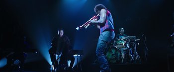 Movie still from “Miles Ahead” (2015), directed by Don Cheadle – A man playing the trumpet on a stage with other musicians; Wide shot, Low angle