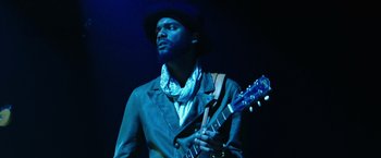 Movie still from “Miles Ahead” (2015), directed by Don Cheadle – A man with a hat on holding a blue guitar; Close Up shot, Low angle