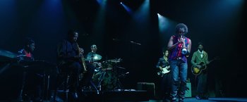 Movie still from “Miles Ahead” (2015), directed by Don Cheadle – A group of people on a stage playing musical instruments; Wide shot, Low angle