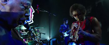 Movie still from “Miles Ahead” (2015), directed by Don Cheadle – A man playing a musical instrument while another man plays a guitar; Medium shot, Low angle