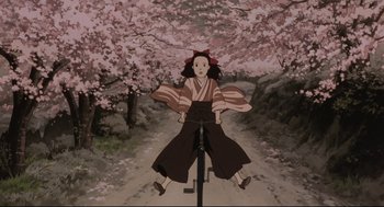 Movie still from “Millennium Actress” (2001), directed by Kô Matsuo – A girl riding a bike in front of a tree filled with pink flowers; Wide shot, Low angle