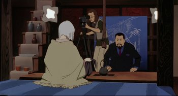 Movie still from “Millennium Actress” (2001), directed by Kô Matsuo – A man sitting in front of another man in front of a camera; Medium shot, Over the shoulder angle
