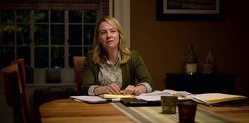 Movie still from “13 Reasons Why” (2017), created by Brian Yorkey – A woman sitting at a table with papers; Medium shot, Over the shoulder angle