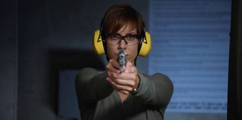 Movie still from “13 Reasons Why” (2017), created by Brian Yorkey – A woman wearing ear muffs and holding a gun; Medium shot, Low angle