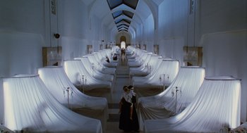 Movie still from “Mimic” (1997), directed by Guillermo del Toro – A woman walking down a staircase in a room; Extreme Wide shot, High angle