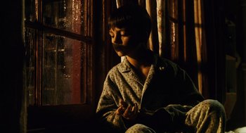 Movie still from “Mimic” (1997), directed by Guillermo del Toro – A young boy sitting on a couch in front of a window; Medium shot, High angle