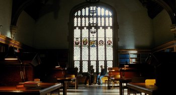 Movie still from “Mimic” (1997), directed by Guillermo del Toro – Two people sitting in front of a stained glass window in a library; Extreme Wide shot, High angle