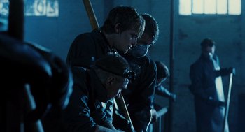 Movie still from “Mimic” (1997), directed by Guillermo del Toro – A group of men sitting next to each other in a dark room; Medium shot, Low angle
