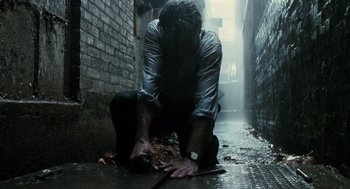 Movie still from “Mimic” (1997), directed by Guillermo del Toro – A man kneeling on the ground in the middle of a dark alley; Medium shot, Low angle