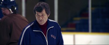 Movie still from “Miracle” (2004), directed by Gavin O'Connor – A man in a blue jacket is standing on a hockey rink; Medium shot, Low angle