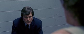 Movie still from “Miracle” (2004), directed by Gavin O'Connor – A man wearing a suit and tie sitting in front of a brick wall; Close Up shot, Over the shoulder angle