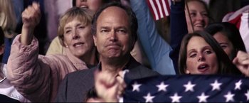 Movie still from “Miracle” (2004), directed by Gavin O'Connor – A man with a frowning look on his face in front of an american flag; Close Up shot, Over the shoulder angle