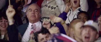 Movie still from “Miracle” (2004), directed by Gavin O'Connor – A group of people sitting in a crowd with their hands up; Medium shot, High angle