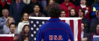 Movie still from “Miracle” (2004), directed by Gavin O'Connor – A man in a blue jacket stands in front of an american flag; Medium shot, Over the shoulder angle