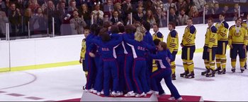 Movie still from “Miracle” (2004), directed by Gavin O'Connor – A group of men in blue and red sports uniforms hugging; Wide shot, High angle