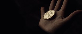 Movie still from “Miracle at St. Anna” (2008), directed by Spike Lee – A hand is holding a coin that says " herb 5 louisiana ice slops " on it; Extreme Close Up shot, High angle