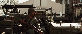 Movie still from “Miracle at St. Anna” (2008), directed by Spike Lee – A man holding a rifle sitting in front of a building; Medium shot, Low angle