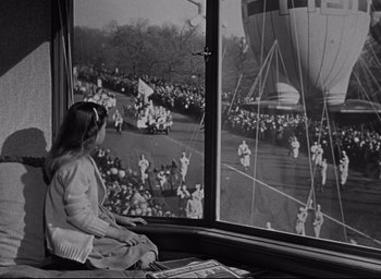 Movie still from “Miracle on 34th Street” (1947), directed by George Seaton – A girl sitting in front of a window looking out at a parade; Wide shot, High angle
