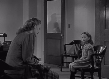 Movie still from “Miracle on 34th Street” (1947), directed by George Seaton – A woman and a girl sitting on a chair in front of a door; Wide shot, Over the shoulder angle