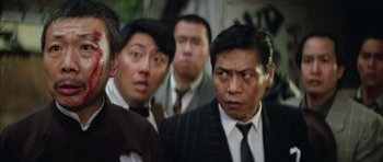 Movie still from “Miracles: The Canton Godfather” (1989), directed by Jackie Chan – A group of men in suits and ties standing next to each other; Close Up shot, Over the shoulder angle