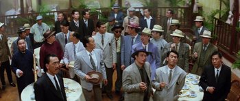 Movie still from “Miracles: The Canton Godfather” (1989), directed by Jackie Chan – A group of men in suits and hats standing in a room; Wide shot, High angle