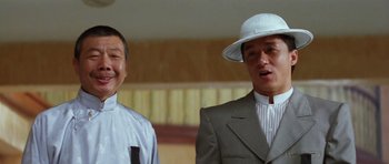 Movie still from “Miracles: The Canton Godfather” (1989), directed by Jackie Chan – Two men in suits and a white hat are smiling for the camera; Close Up shot, Low angle