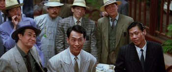 Movie still from “Miracles: The Canton Godfather” (1989), directed by Jackie Chan – A group of men in suits and hats standing next to each other; Medium shot, Over the shoulder angle