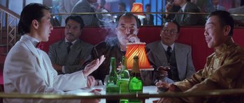 Movie still from “Miracles: The Canton Godfather” (1989), directed by Jackie Chan – A group of men sitting at a table with drinks; Medium shot, Over the shoulder angle