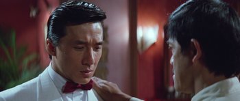 Movie still from “Miracles: The Canton Godfather” (1989), directed by Jackie Chan – A man in a red bow tie is looking down at his shoulder; Close Up shot, Over the shoulder angle