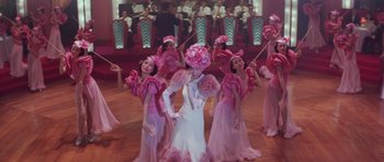 Movie still from “Miracles: The Canton Godfather” (1989), directed by Jackie Chan – A group of women in pink dresses and hats performing; Wide shot, Low angle
