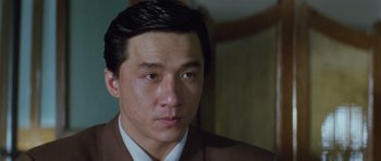 Movie still from “Miracles: The Canton Godfather” (1989), directed by Jackie Chan – A person wearing a suit and tie; Close Up shot, Low angle