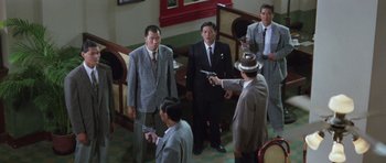 Movie still from “Miracles: The Canton Godfather” (1989), directed by Jackie Chan – A group of men in suits holding guns in a room; Wide shot, High angle