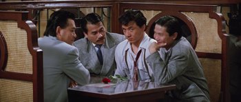 Movie still from “Miracles: The Canton Godfather” (1989), directed by Jackie Chan – A group of men sitting at a table with a red rose; Medium shot, High angle