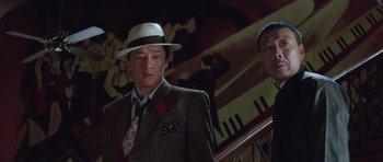 Movie still from “Miracles: The Canton Godfather” (1989), directed by Jackie Chan – A man wearing a hat and a suit and tie; Close Up shot, Low angle