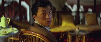 Movie still from “Miracles: The Canton Godfather” (1989), directed by Jackie Chan – A person sitting in a chair; Close Up shot, Over the shoulder angle
